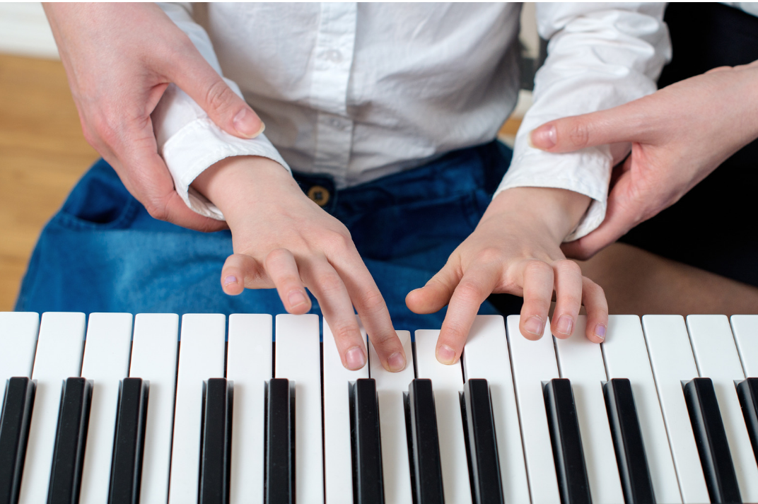 Teacher guiding boy's hands on piano keyboard, importance of reading music notes