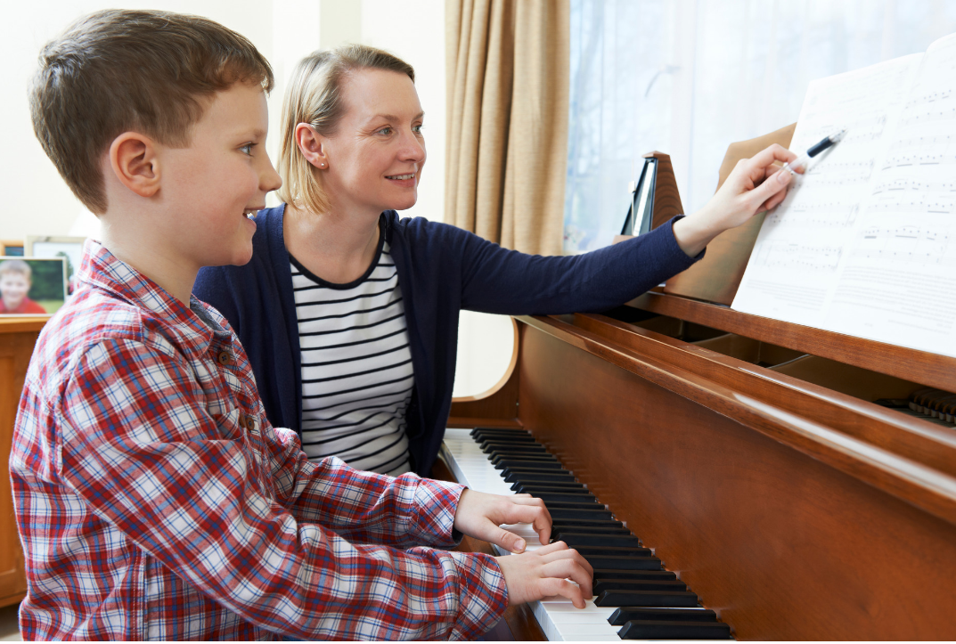 Boy In Plaid Shirt Practicing Piano As Teacher Points To Sheet Music, Learn Why Practice Is Not About Perfections It's About Progress