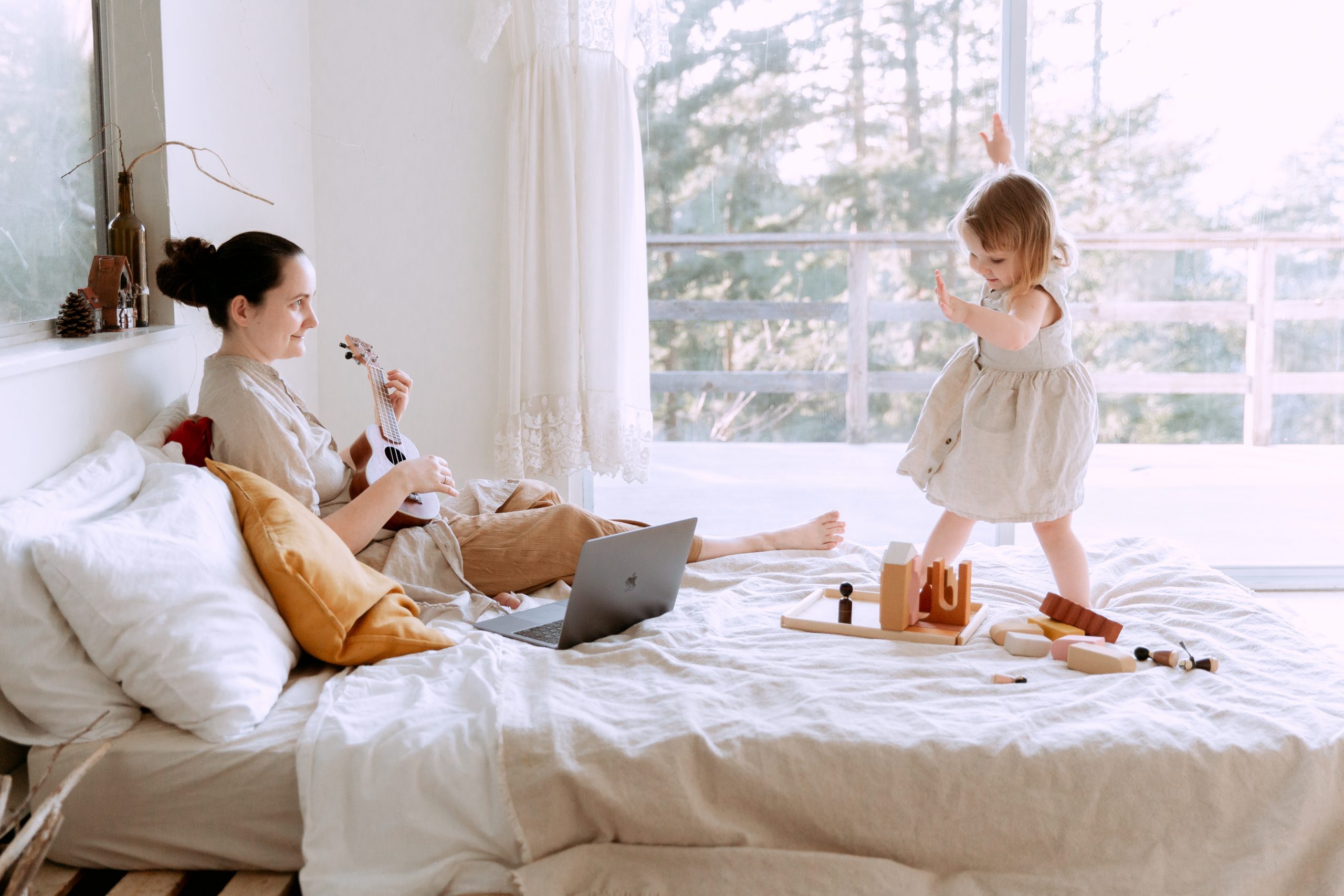 Mom Playing Ukulele While Little Girl Dances On The Bed, Learn How To Bring Music Lessons To Your Homeschool For Free