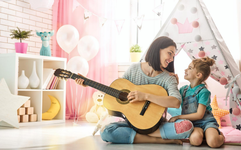 Mom And Primary School Aged Daughter With Guitar In Homeschool Learning About Different Genres Of Music